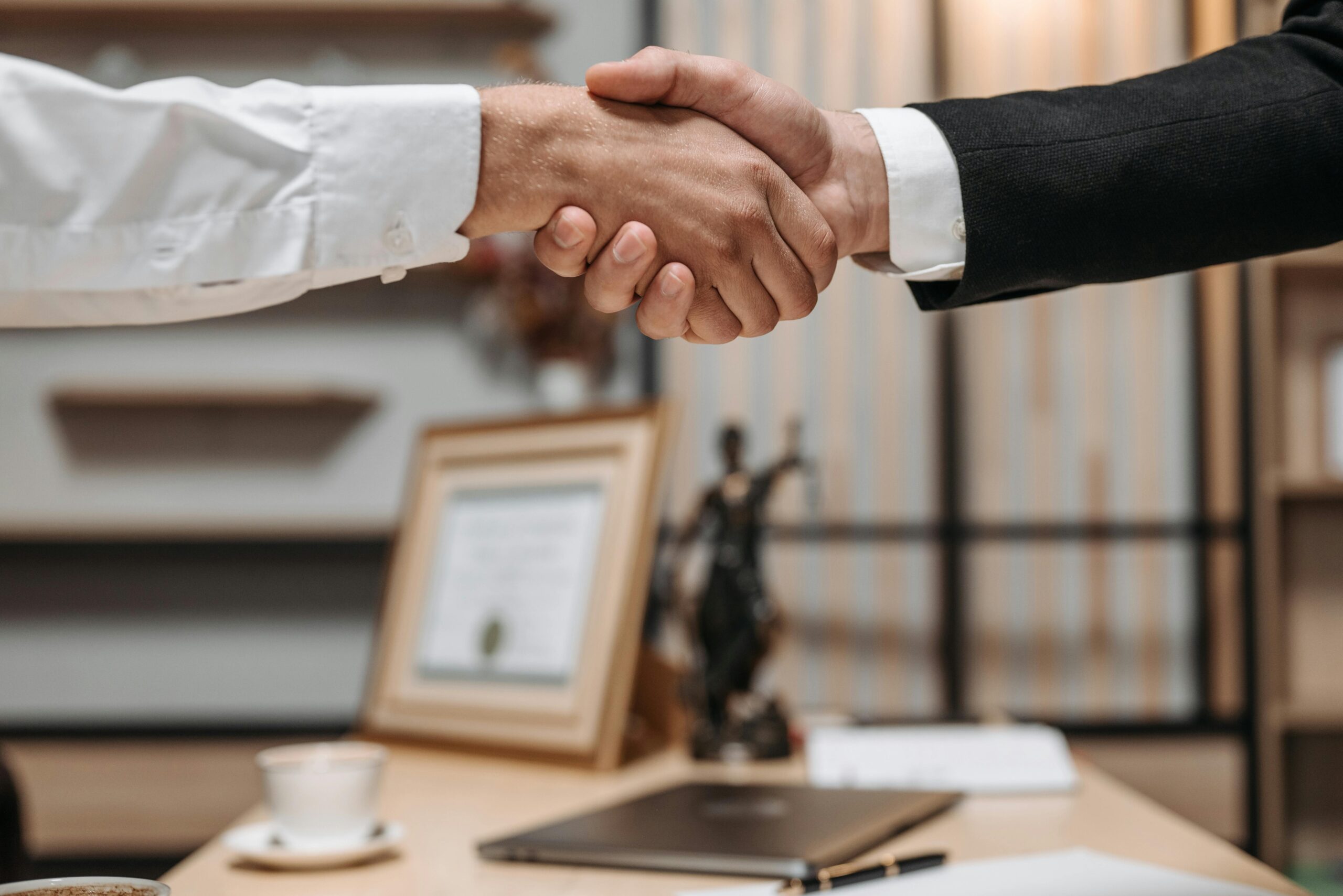 Close-up of a handshake between two professionals in a modern office setting, emphasizing partnership and agreement.